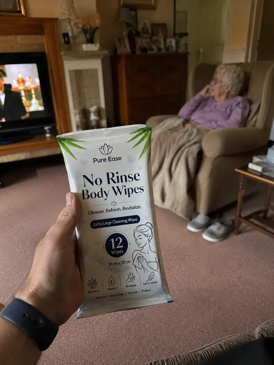 PureEase body wipes held in a living room with an older person seated in the background.