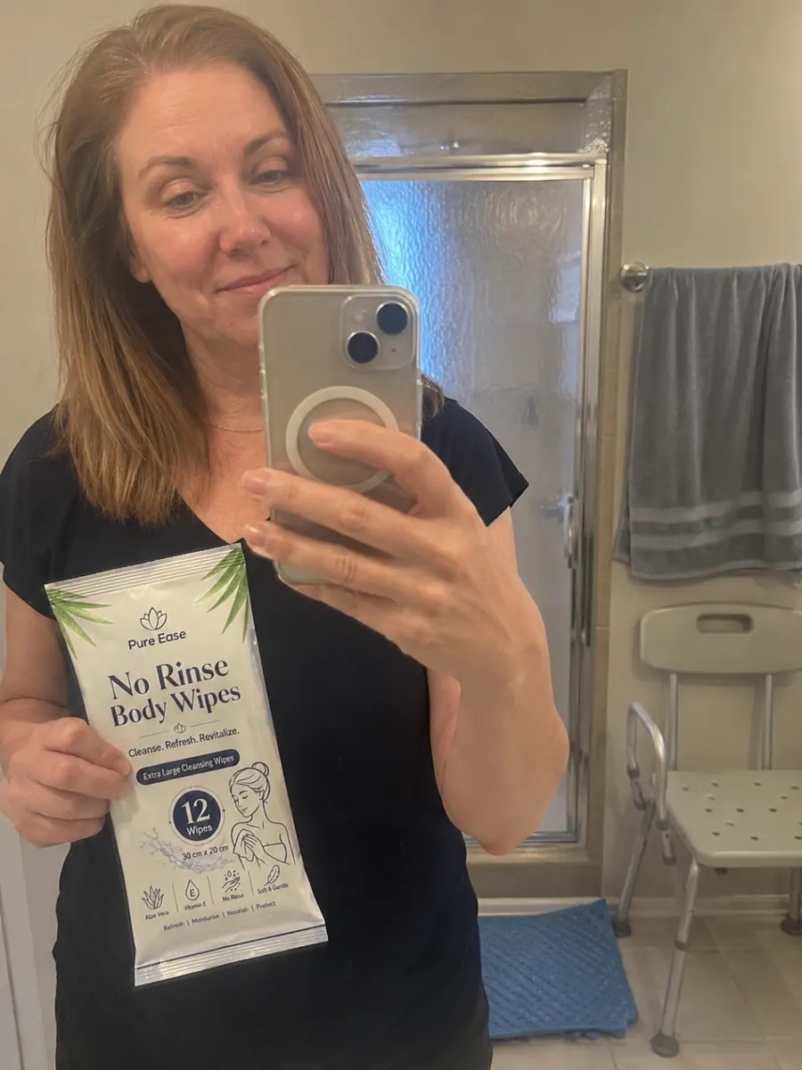 Customer holding PureEase No Rinse Body Wipes in a bathroom mirror selfie.