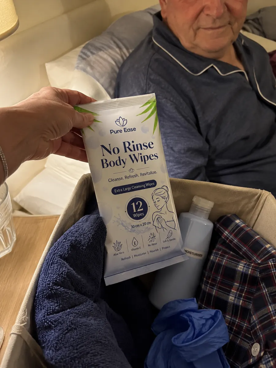 PureEase body wipes held above a bedside care basket next to an older man in bed.